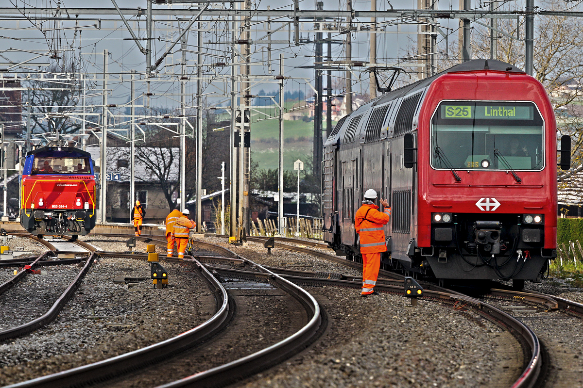 Ein Securitrans Bahnwächter begrüsst die durchfahrende S25 ohne Nummer während eine Gleiskontrollrotte der Arbeit nachgeht,Eem 923 024-4 rangiert nebenbei auf einem Seitengeleise.Bild vom 7.11.2014 Reichenburg