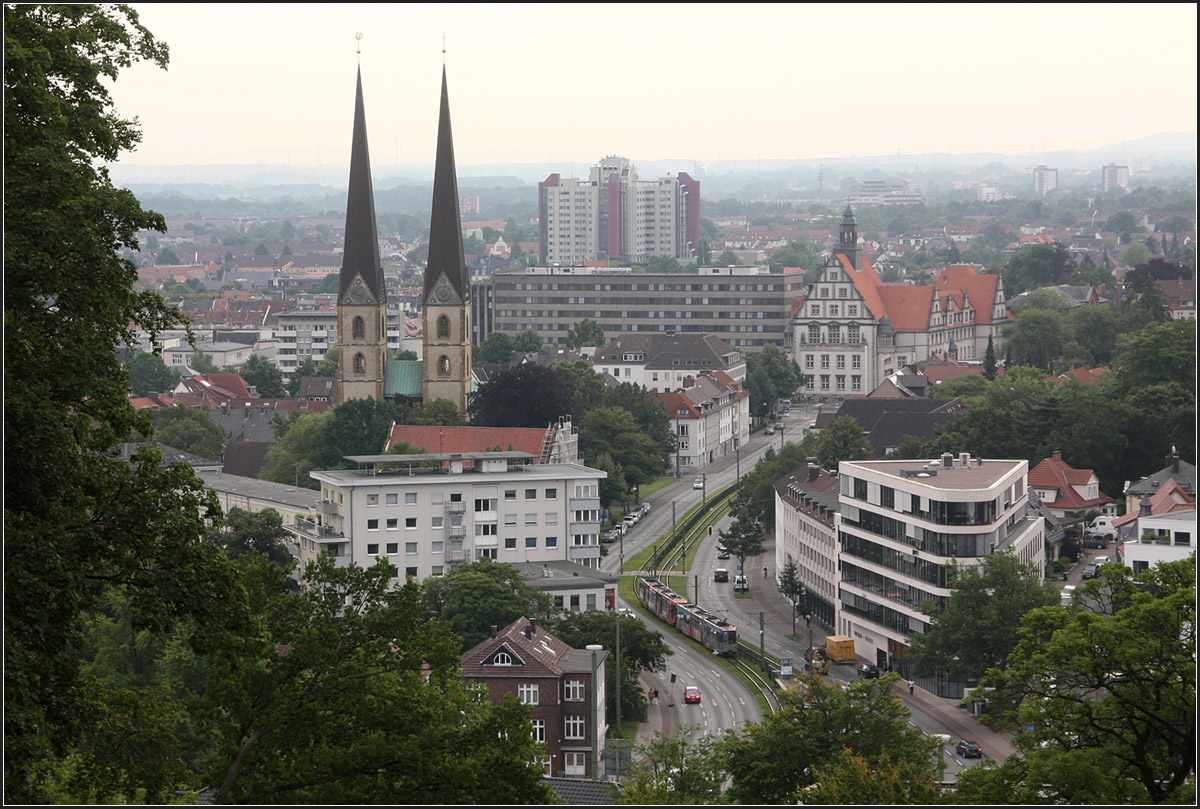 Ein Städtefoto mit Stadtbahn -

Blick vom Hang des Johannisberges auf Bielefeld mit den spitzigen Türmen der Neustädter Marienkirche und dem Landgericht rechts. Auf der Kreuzstraße ist ein Stadtbahnwagen M unterwegs in den Süden der Stadt. 

10.08.2015 (M)