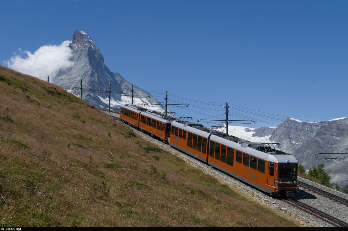 Ein Zug der GGB fährt am 31. Juli 2015 vor der Kulisse des Matterhorns, bei dem am Mittag bereits Wolken aufziehen, auf der Doppelspur oberhalb der Riffelalp talwärts.