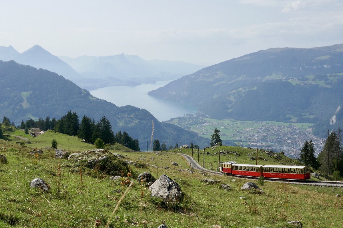 Ein Zug der Schynigen Platte Bahn auf der Talfahrt nach Wilderswil, am 26.8.17 oberhalb von Breitlauenen, mit grandiosem Ausblick auf den Thunersee, Niesen und die Stadt Interlaken.
