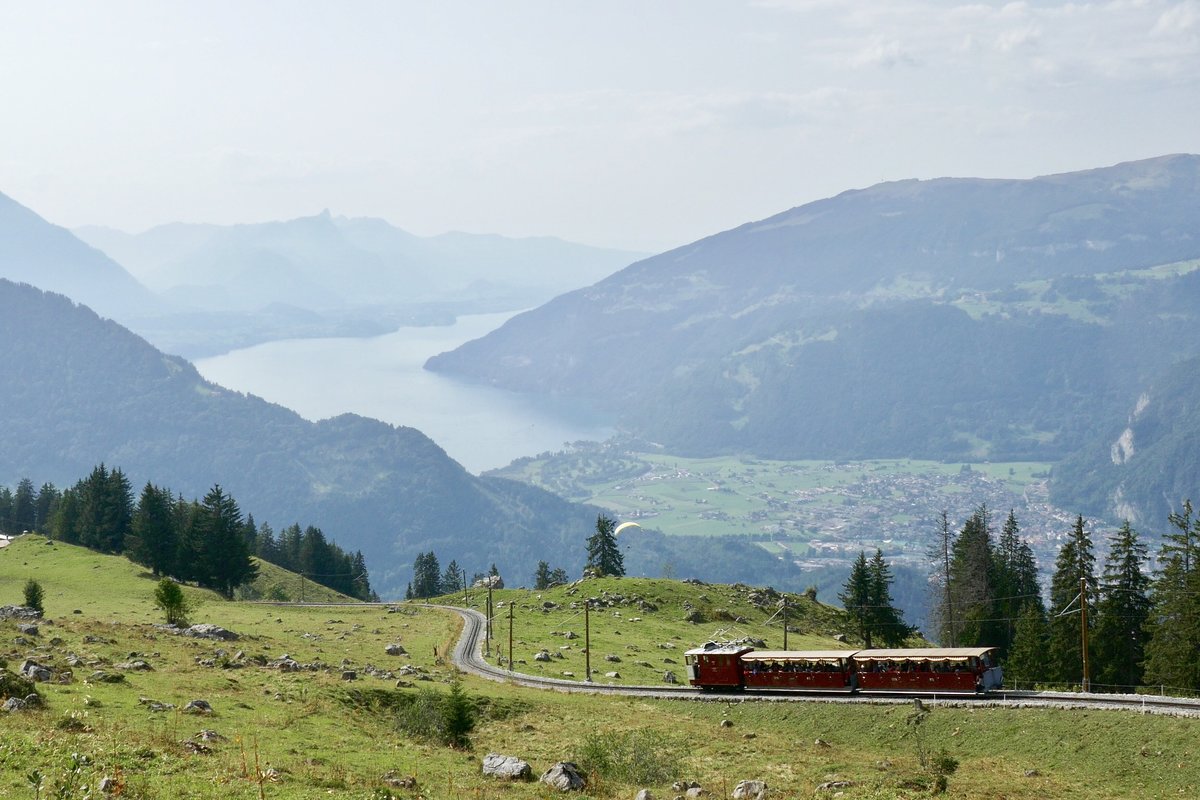 Ein Zug der Schynigen Platte Bahn mit offenen Wagen am 26.8.17 auf dem Weg ins Tal nach Wilderswil, mit bestem Ausblick auf den Thunersee und Interlaken oberhalb von Breitlauenen.