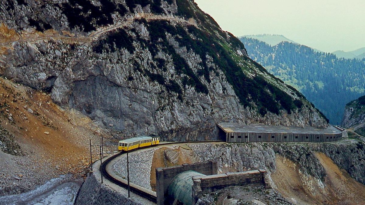 Ein Zug der Wendelsteinbahn überquert im Sommer 1976 die Hohe Mauer. Im Vordergrund der Tunneleingang zur Bergstation, die nach Durchfahren einer 180-Grad-Kurve erreicht wird.