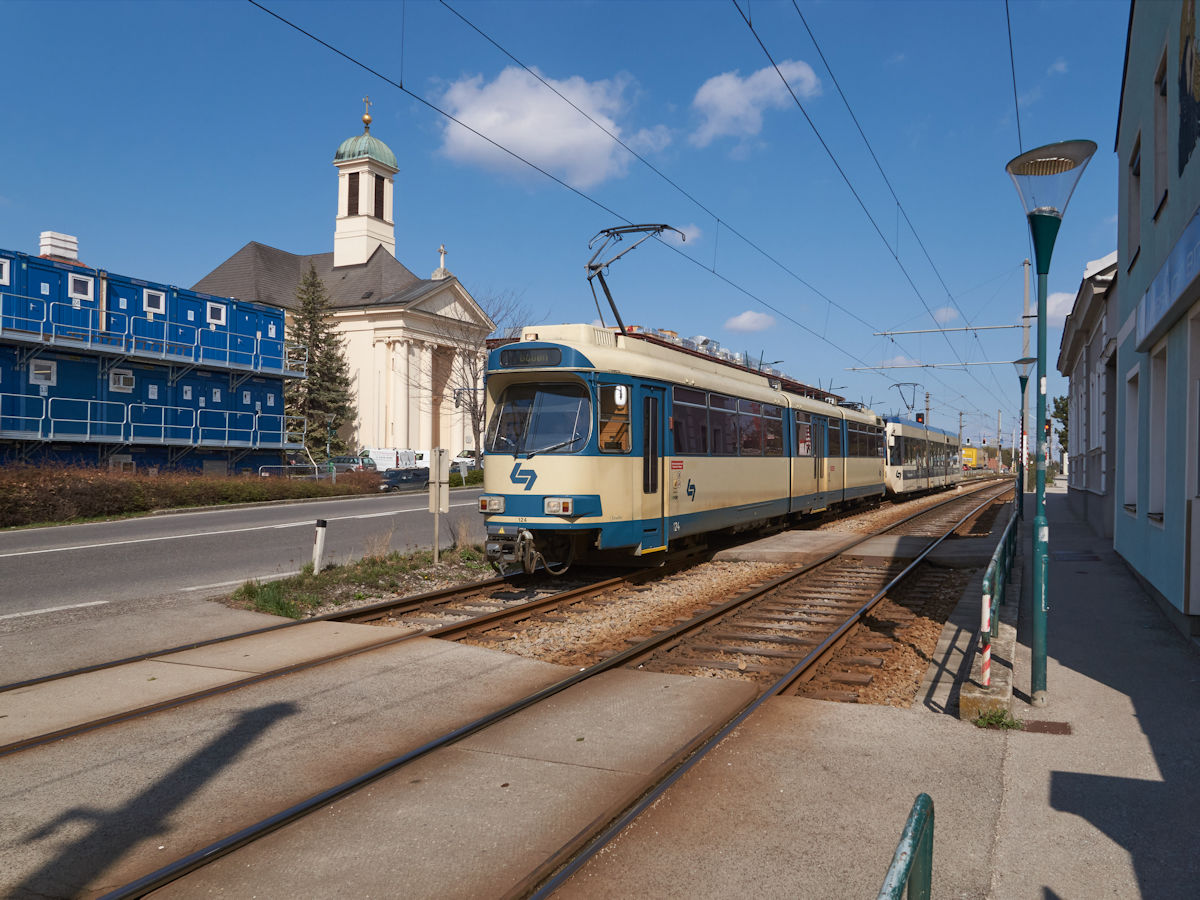 Ein Zug der Wiener Lokalbahn, bestehend aus Tw 124 und einem Triebwagen der 400er Reihe, fuhr am 04.04.2022 durch Wiener Neudorf nach Baden. Kurz nach dem Bahnhof Wiener Neudorf fährt er an der Katholischen Kirche vorbei. 