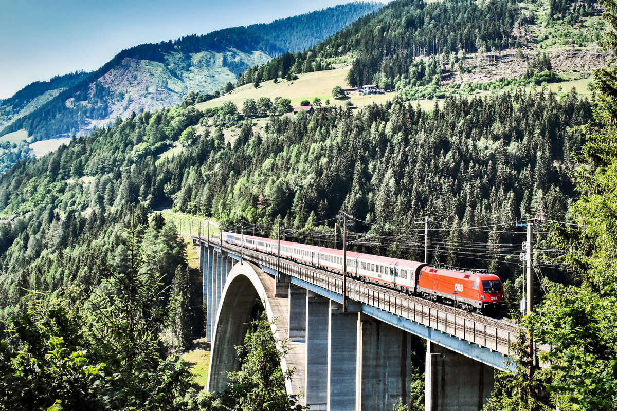 Eine 1116 überquert mit dem EC 113  Blauer Enzian  (Frankfurt (Main) Hbf - Klagenfurt Hbf/ - Zagreb Glavni kol.) die Pfaffenberg-Zwenberg-Brücke bei Penk.
Aufgenommen am 30.6.2019.