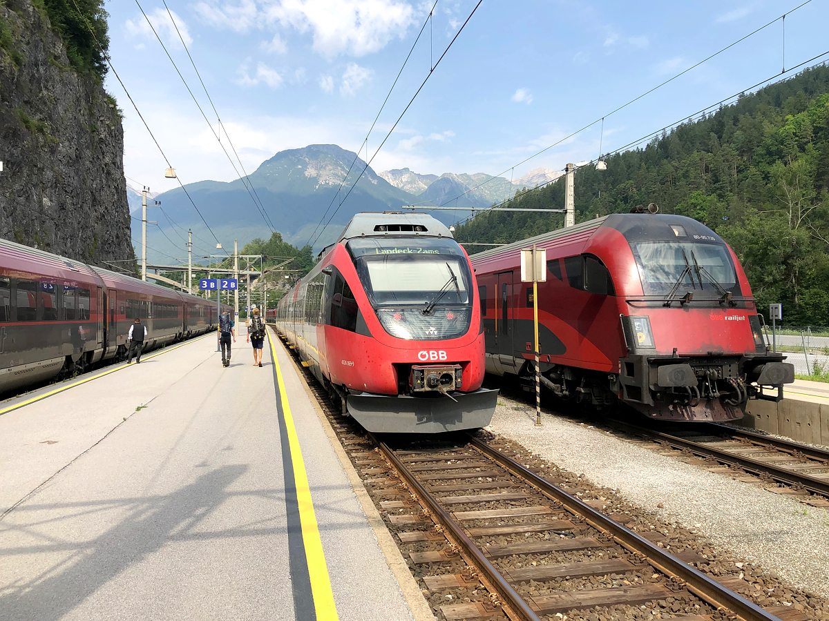 Eine 3fache Zugkreuzung am nur 4 gleisigen Bahnhof Imst-Pitztal. Immer Samstag im Sommer und Winter kreuzen sich hier am Vormittag der samstäglichen Zusatz RailJet 1286/1287 (von Feldkirch nach München Hbf und retour) auf Gleis 3 (links) und ein REX nach Landeck-Zams auf Gleis 2 (Mitte). Ebenfalls muss der Zusatz RailJet 1286/1287 den RailJet 865 (rechts) auf Gleis 1 nach Wien Hbf überholen lassen. Aufgenommen am 24.07.2021