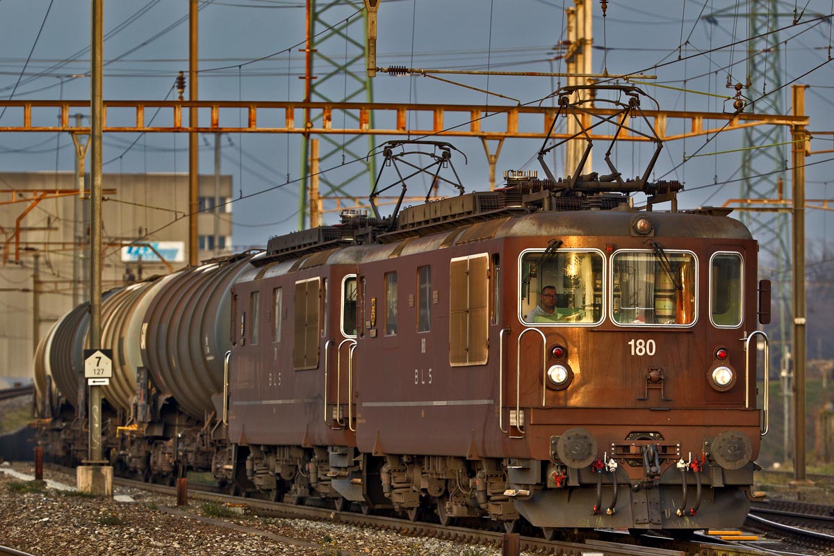 Eine Doppeltraktion bestehend aus der Re 425 180  Ville de Neuchatel  und der Re 425 171  Därligen  taucht im ersten Morgenlicht mit einem Kesselwagenzug im Bahnhof Pratteln auf.Bild vom 7.12.2016