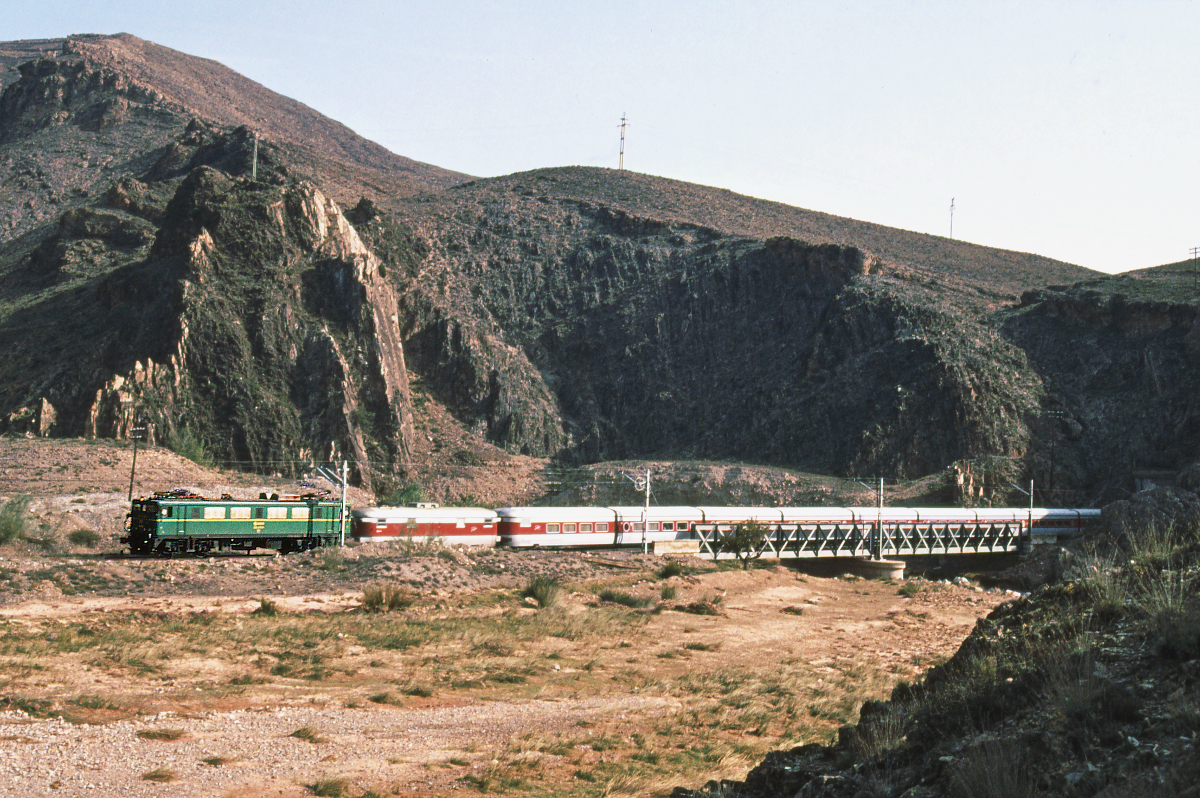 Eine Elok der Reihe 269 führt den Talgo 172 von Madrid Chamartin über Zaragoza und Tarragona nach Barcelona Termino. Madrid hat er um 11.25 verlassen, wir sehen in kurz hinter Calatayud, wo er knapp drei Stunden später um 14.10 gehalten hat. Barcelona erreicht er nach 687 km Fahrt um 19.59. Ein spanischer Hochgeschwindigkeitszug benötigt heute (2020) für diese Strecke gerade einmal 2,5 Stunden.
Oktober 1983. Canon AE1, Canoscan, GIMP. 