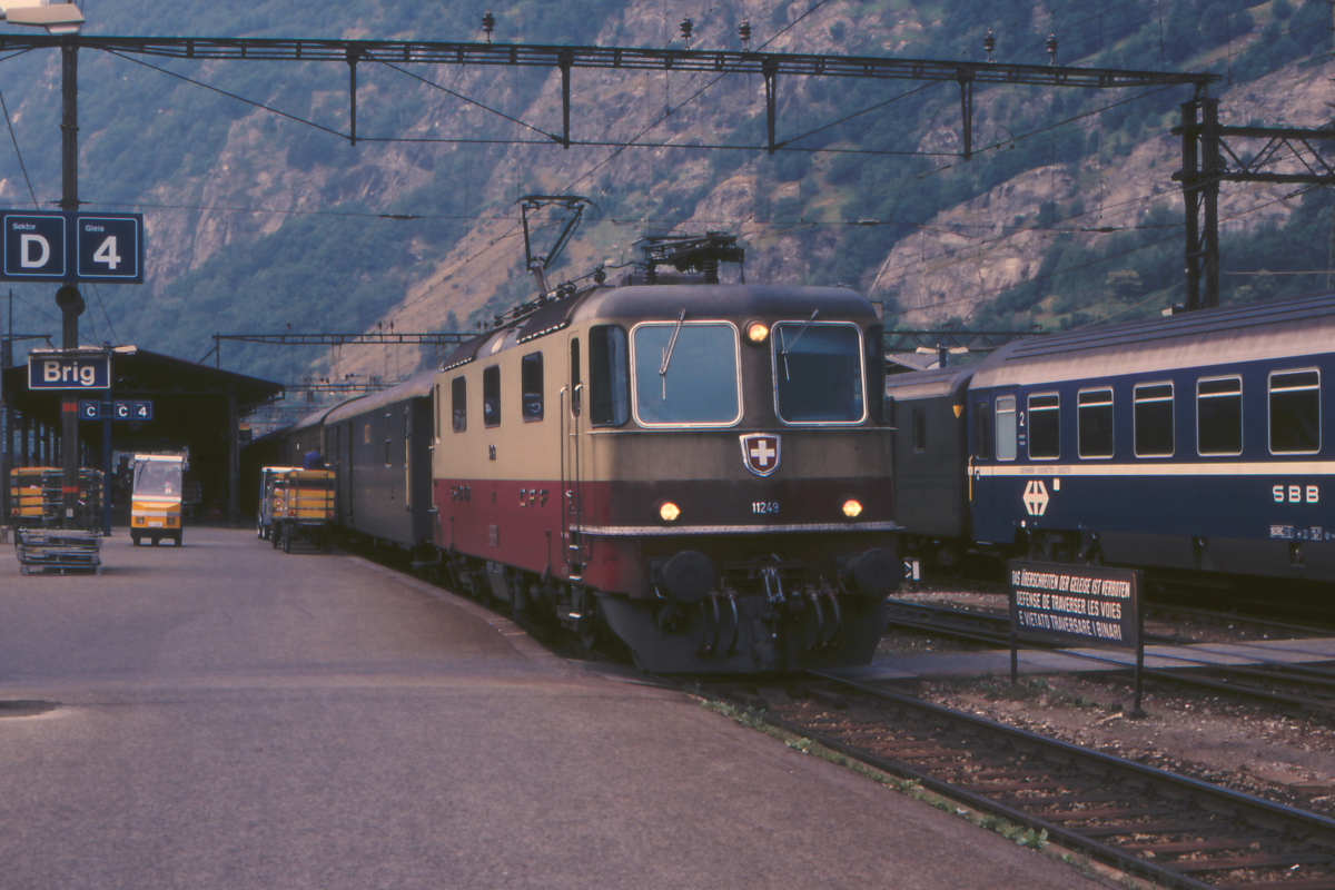 Eine der gelungensten konventionellen Elektrolok-Baureihen ist die Re 4/4 II der SBB. 
Hier steht die TEE-farbene 11249 mit einem Zug aus Einheitswagen II im Bahnhof Brig im Rhone-Tal. 
28. Juni 1988; 
Canon AE1, Canoscan, Gimp
