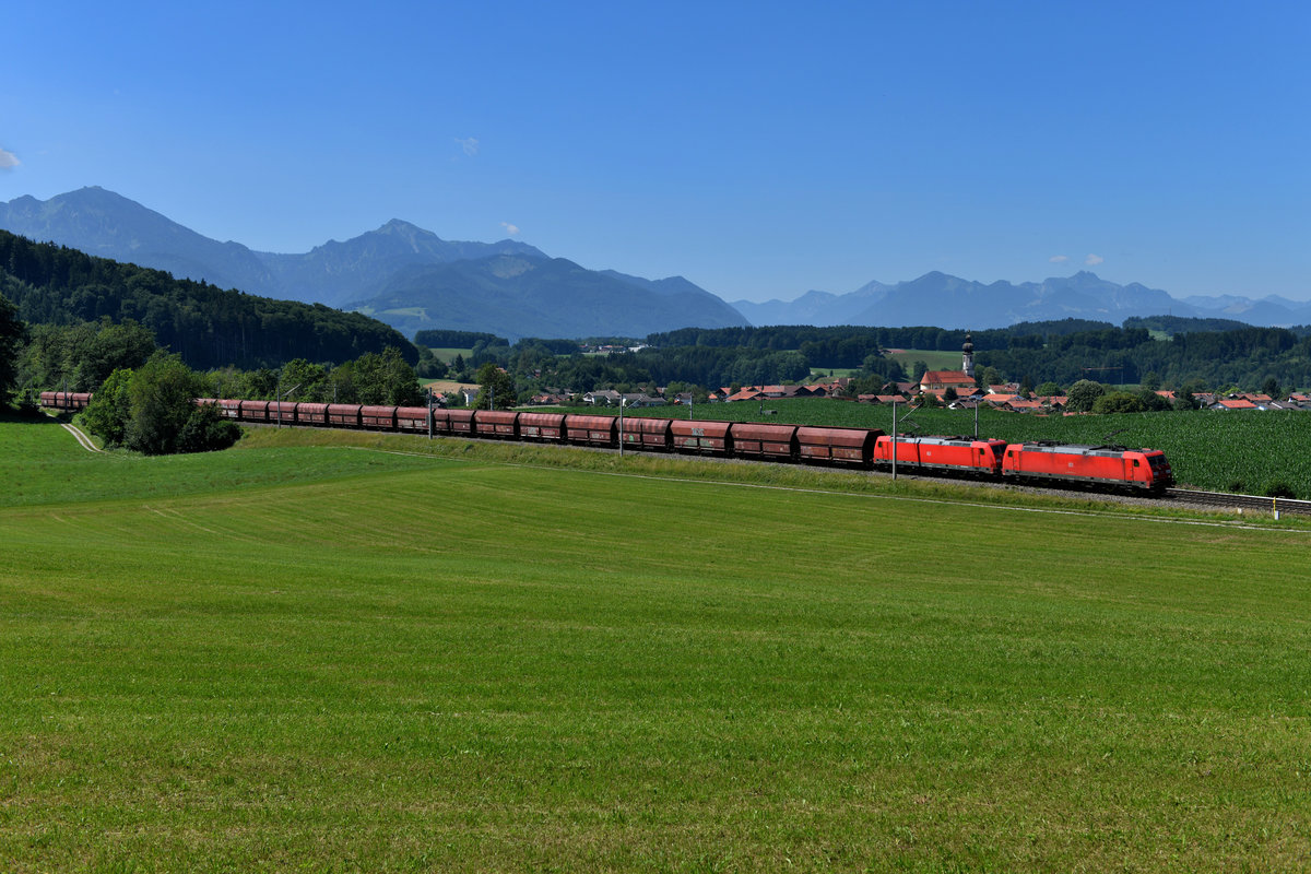 Eine konstante Größe auf der Passauerbahn sind die schweren Erzzüge zum Werk der Voest. Aufgrund einer baustellenbedingten Sperre dieser Strecke wurden Ende Juli diese Leistungen über München und Salzburg umgeleitet. Am 23. Juli 2019 konnte ich bei Axdorf den GM 47923 von Neuss Gbf nach Linz Stahlwerke, geführt von 185 296 und 320, mit den Chiemgauer Alpen im Hintergrund fotografieren. Zu meiner Überraschung passte hier sogar der komplette Zug auf das Bild. Von links gesehen erkennt man den Hochgern und den Hochfelln, rechter Hand in der Ferne die Kampenwand sowie die Ortschaft Vachendorf mit der Kirche Mariä Himmelfahrt. Hinweis: Auch hier wurden einige störende Hochspannungsleitungen digital entfernt.  