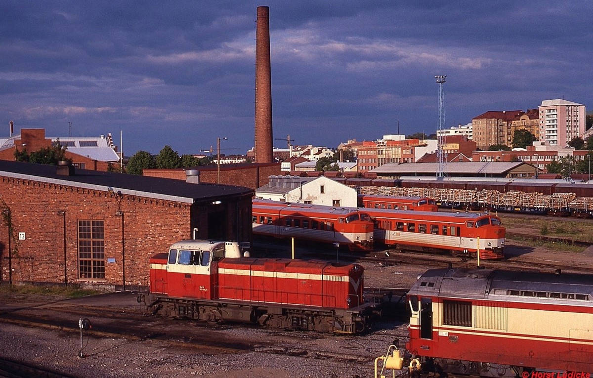 Eine Lokomotive der Reihe Dv12 im Juni 1990 in Jyvskyl. Rechts vorne eine Lokomotive der Reihe Dr13, im Hintergrund sind mehrere Triebwagen der Reihe Dm8/Dm9 abgestellt. Die Dv12 ist technisch mit der deutschen BR 212 verwandt, ihre Drehgestelle sind mit denen der deutschen V 160 identisch. Sie kann dank ihres Stufengetriebes sowohl im Gterverkehr mit 80 km/h bzw. im Personenverkehr mit 125 km/h eingesetzt werden.