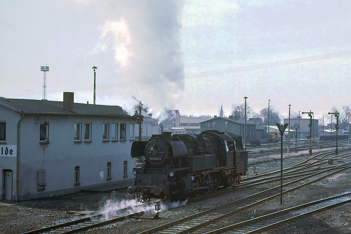 Eine Neubaudampflok der DR, genau die 65 1043, rangiert im Bahnhof Leinefelde. Bei diesen Lokomotiven beeindruckte mich stets die kompakte Bauweise, die hohe Kessellage und das insgesamt moderne Aussehen. Aber 1976 war der Stern dieser Baureihe schon im Sinken. Ich erinnere mich,daß die Lok nur noch gelegentlich zwischen Nordhausen und Leinefelde vor Personenzügen zum Einsatz kamen. Reisezüge wurden meist von Diesellok der Baureihen 110 und 180 gefahren, nur vor Güterzügen kamen noch regelmäßig Dampflok der Reihe 44 zum Einsatz. April 1976, Leinefelde, damalige DDR