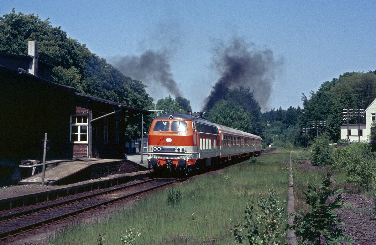 Eine nicht gerade klimafreundliche Anfahrt legt 218 143 am 15.6.1986 am Hp. Kotthausen hin. Links erkennt man die klägliche Überreste des ehemals stattlichen Bahnhofsgebäudes und rechts das Gleisbett von weiteren ehemaligen Bahnhofsgleisen.