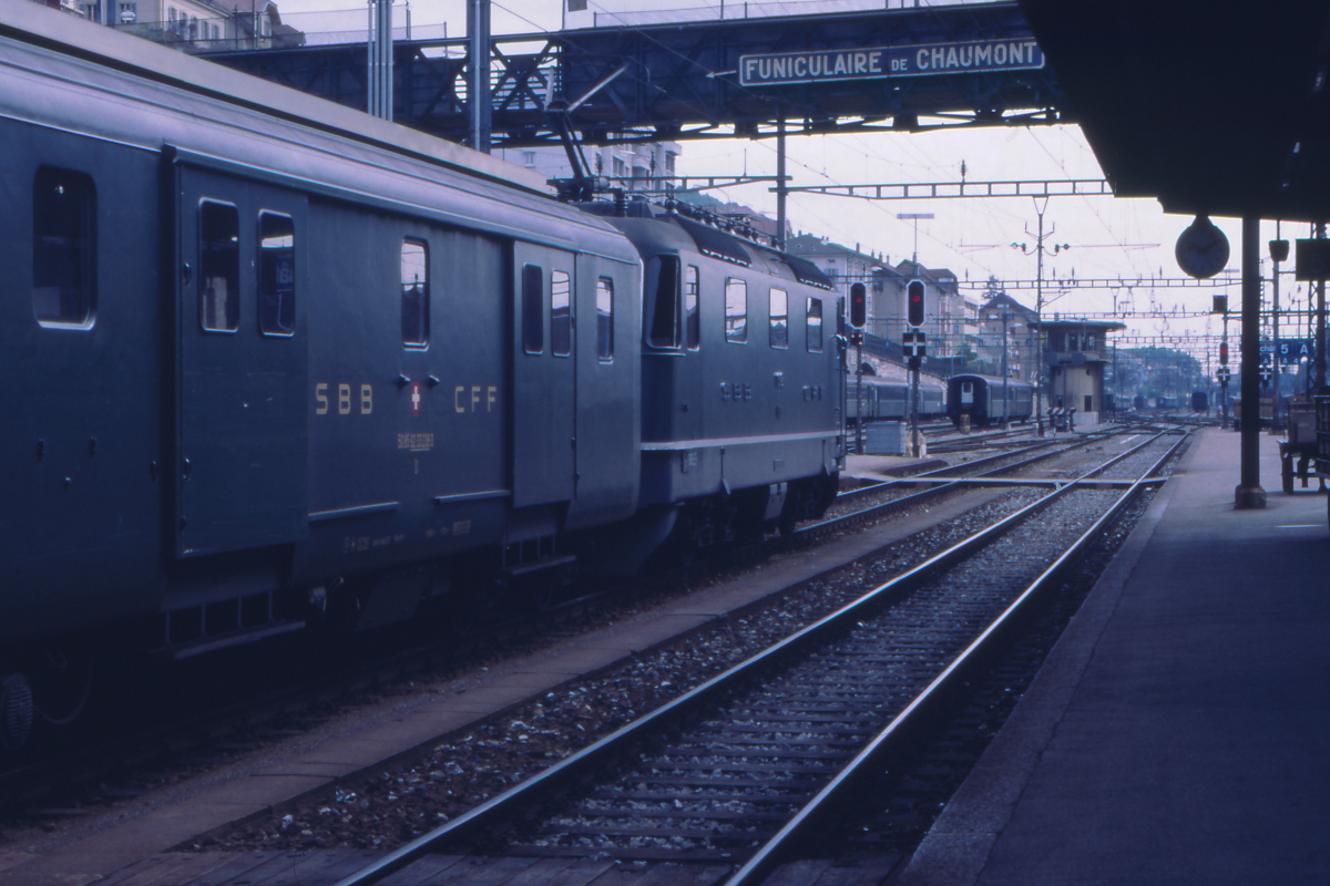 Eine Re 4/4 II der SBB, vielleicht die 11343 (die Nummer ist nicht eindeutig zu erkennen), wartet im Bahnhof Neuchatel auf Weiterfahrt Richtung Biel. Hinter der Lok ist ein Gepäckwagen eingereiht. Nicht nur in der Schweiz waren Gepäckwagen über viele Jahrzehnte der Normalfall, hatte ein Zug keinen Gepäckwagen, wurde im Kursbuch darauf hingewiesen. Die SBB erwarb in den 1980er Jahren sogar überzählige Gepäckwagen der SNCF, um alle ihre IC damit ausrüsten zu können.
Neuchatel, 6. Juni 1987; canon AE-1, Canoscan, Gimp