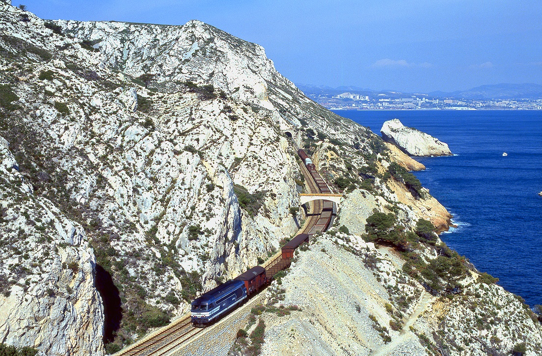 Eine der spektakulrsten Strecken Frankreichs ist die Linie Marseille - Martigues direkt an der Kste. Brcken und Tunnel in stetem Wechsel - und immer mit Blick auf (das im Hintergrund sichtbare) Marseille. Einmal tglich gibt es sogar einen Gterzug auf dieser Linie. BB67568 ist bei Niolon am 06.05.1998 Richtung Martigues unterwegs.