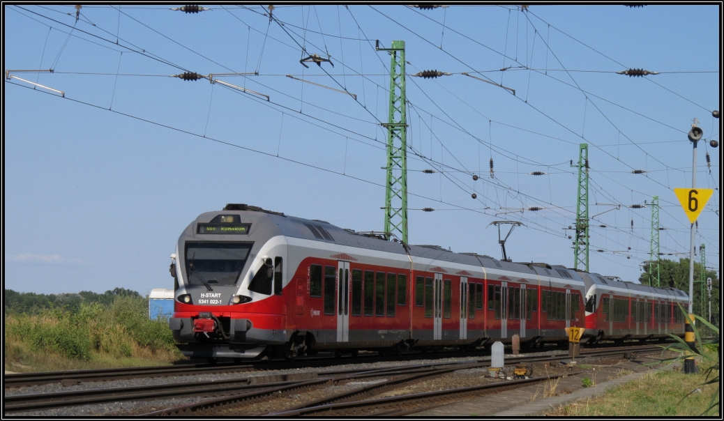 Eine Stadler Flirt Doppelgarnitur der MAV H_Start kommt aus Budapest Deli nach Komárom gefahren. Hier zu sehen am Donauufer am östlichen Ende des Bahnhofs Anfang August 2015.