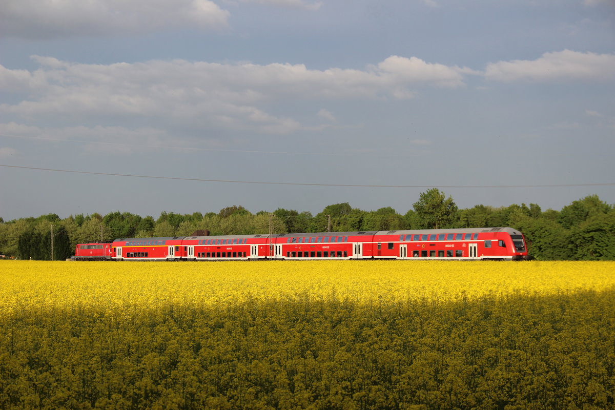Eine unbekannte Schnellzuglok der Baureihe 111 schiebt ihren RE4 Verstärker aus Düsseldorf durch die ländlich geprägte Gegend bei Erkelenz ihrem Ziel Aachen entgegen. Deutlich zu erkennen ist der ehemalige Zugcafe Wagen vor der Lok, welcher ursprünglich auf der RE2 zwischen Mönchengladbach und Münster zu Hause war. 
Erkelenz 2.5.2018