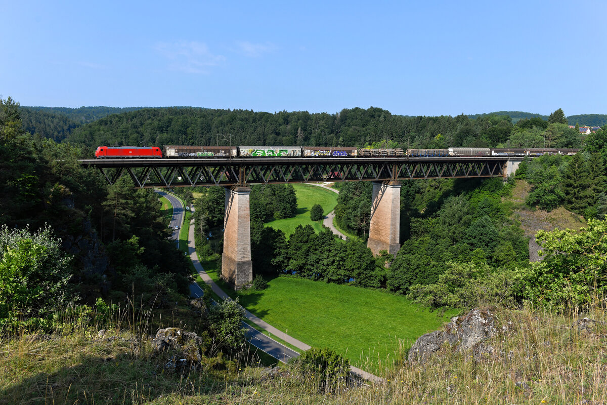 Eine weitwinklige Motivvariation der Beratzhausener Eisenbahnbrücke: Die 185 212 überquert mit einem südwärts fahrenden gemischten Güterzug das Tal der schwarzen Laber (23. Juli 2021).