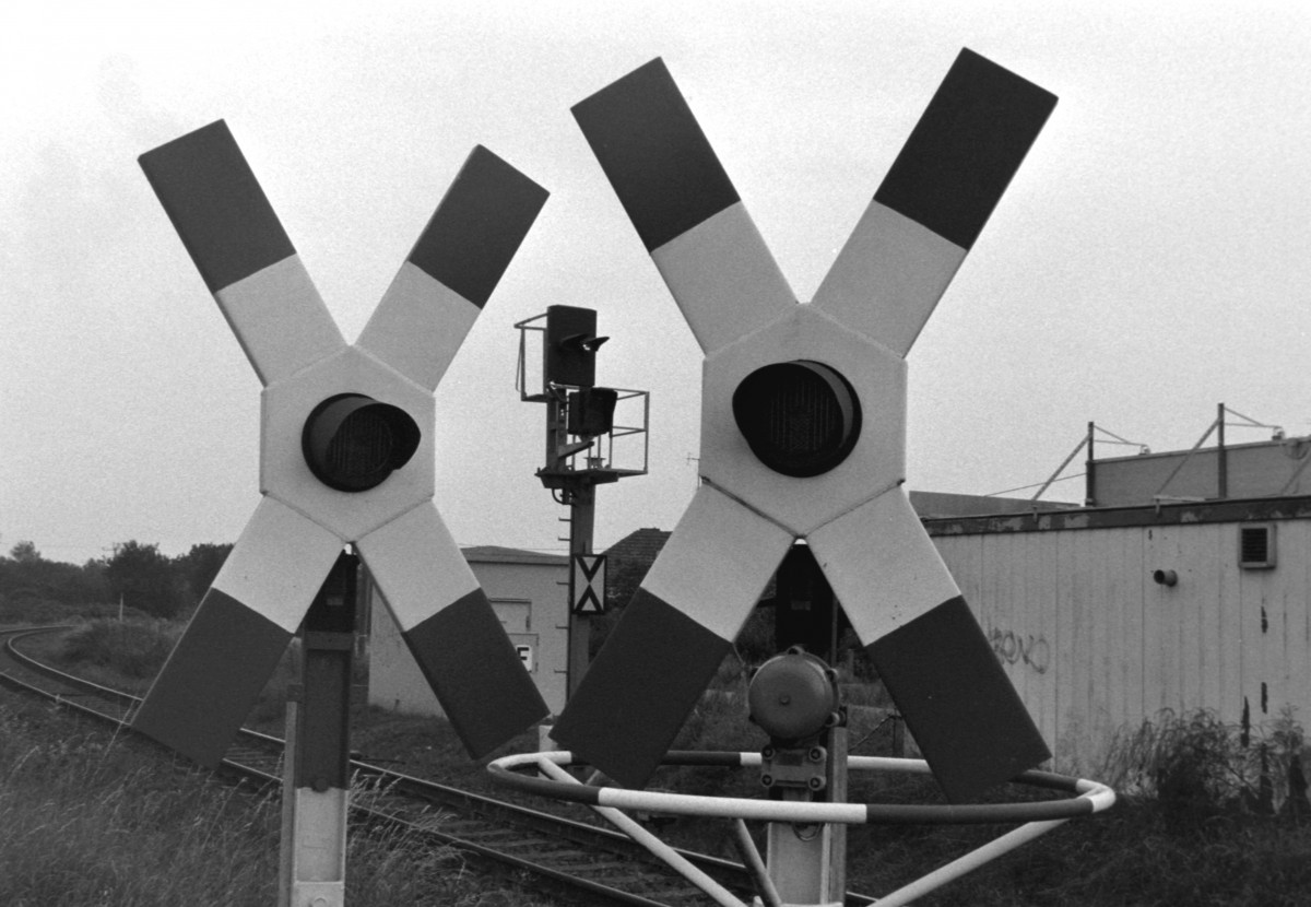 (Eisenbahn-)Welten liegen zwischen den blinkenden Andreaskreuzen der Deutschen Reichsbahn und dem von ihnen eingerahmten Ks-Vorsignal der Deutschen Bahn AG am Bahnbergang  Uelzener Strae  in Salzwedel. Andreaskreuze und Signal haben gemeinsam, dass sie fnf Wochen nach Entstehen dieser Aufnahme vom 23.08.2002 ihre Daseinsberechtigung verloren, da der Gesamtverkehr auf der KBS 301 (Salzwedel–Oebisfelde) eingestellt wurde.