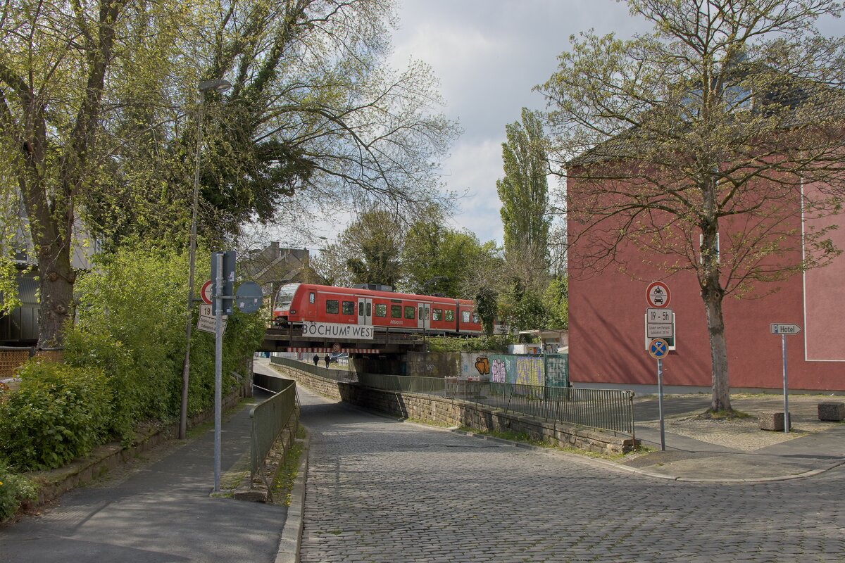 Eisenbahnüberführung an der Gußstahlstraße mit einem typischen Hinweisschild auf den dort gelegenen Haltepunkt Bochum-West; es passiert gerade 426 506-2  Oberlinxweiler  als RB 46 nach Bochum Hbf (22.04.2022)