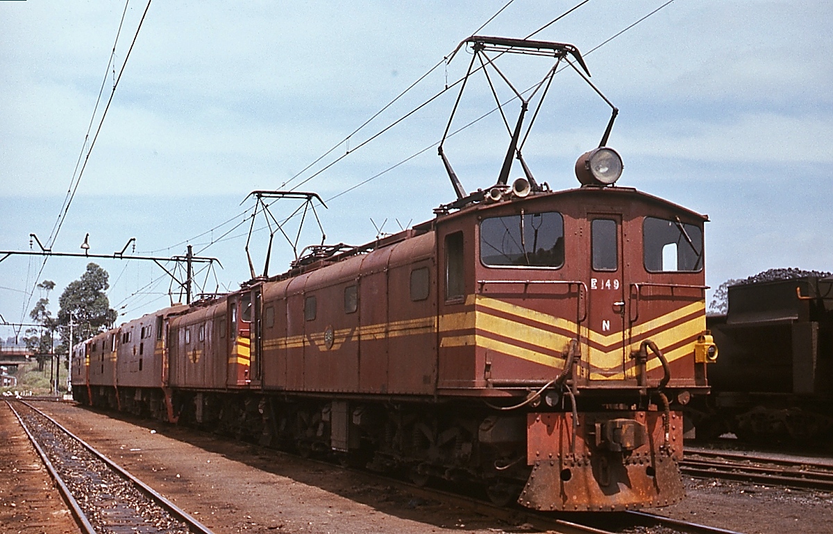 Elektrischer Betrieb in Südafrika im November 1976: In den 1920er Jahren begann die SAR mit der Elektrifizierung ihrer Eisenbahnstrecken. Erste Strecke war die Verbindung von Durban über Pietermaritzburg nach Glencoe. Für den elektrischen Betrieb lieferten verschiedene europäische Hersteller (Metropolitan-Vickers, SLM, Robert Stephenson & Hawthorns, Werkspoor) zwischen 1925 und 1945 insgesamt 172 Lokomotiven der Class 1E. Die im November 1976 in Mason's Mill bei Pietermaritzburg aufgenommene E 149 gehört zur 5. Serie, die von SLM Winterthur (1938) gebaut wurde.