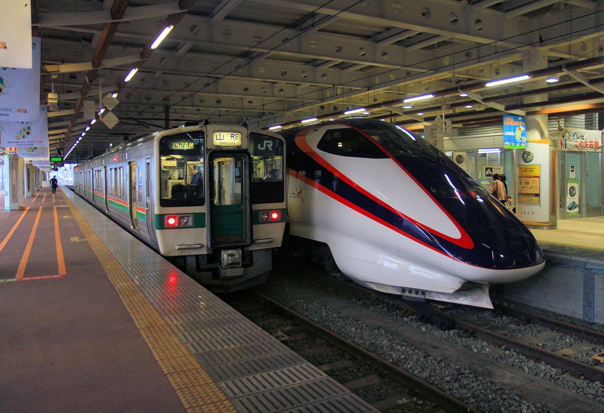 Endstation des Yamagata Shinkansen in der Ortschaft Shinjô im Osten des Yamagata Hochplateaus. Die umgespurte Lokallinie (1067 mm -> 1435 mm) ab Fukushima wird auch von Lokalzügen befahren. Im Bild rechts der Yamagata Shinkansen Zug E3 2012, links ein Lokalzug Serie 719-5000. Shinjô, 17.März 2019 