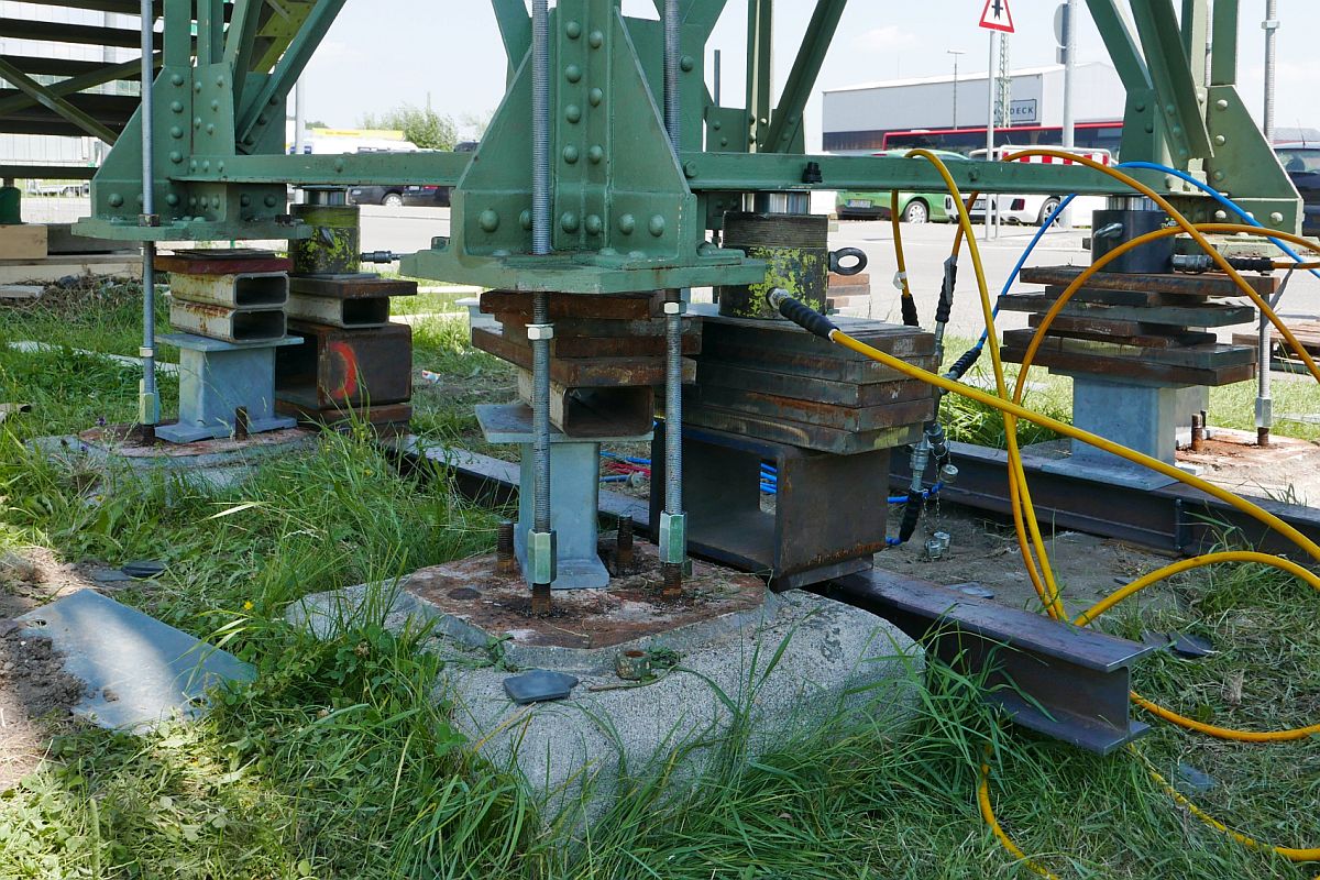 Erh�hung Fu�g�ngersteg in Biberach (Ri�) / (|) - Mit mehreren Hydraulikzylindern verteilt auf alle St�tzen wird der Steg �ber die Bahnlinie Ulm - Friedrichshafen Zentimeter f�r Zentimeter angehoben. Am 27.06.2019 sind von der Erh�hung um 68 cm ca. Zweidrittel geschafft. Aufnahmestandort war der am Steg vorbeif�hrende und nicht abgesperrte Gehweg.