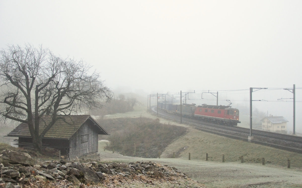 Es herrscht noch trüber Morgennebel, als die Re 6/6 11671 zusammen mit der grünen Re 4/4 II 11330 mit einem Containerzug bei Silenen die letzten Meter der Gotthard-Nordrampe hinunter rollen. 07.12.2016