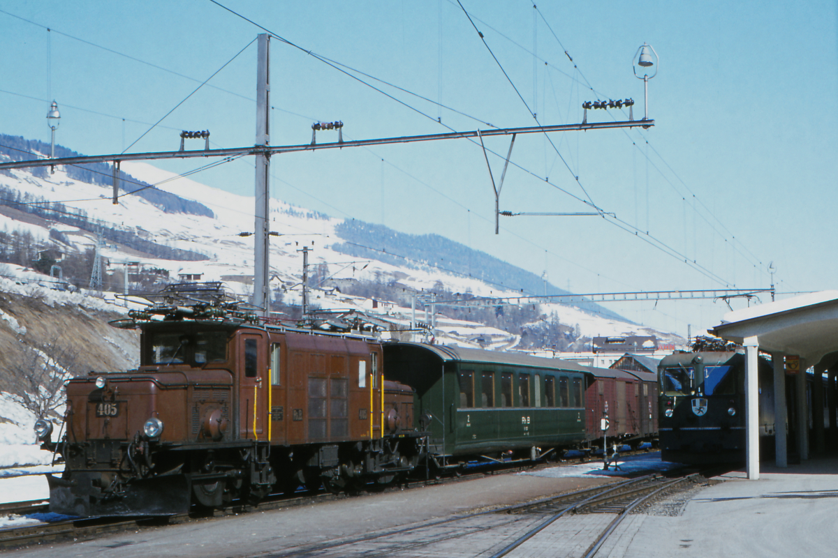 Es ist der Winter 1979, ich fuhr mit meinen Eltern zum Skifahren in die Schweiz. Ich konnte sie überreden, in Scuol-Tarasp anzuhalten, um die Rhätische Bahn zu fotografieren. Das  Krokodil  der Rhätischen Bahn kannte ich schon, mehr wußte ich damals noch nicht. Links steht Ge 6/6 I 405 - ich denke sogar mit einem Gmp, einem Güterzug mit Personenbeförderung. Rechts steht die moderne Ge 4/4 II 616  Filisur  mit einem Zug nach St. Moritz. 
Für das Skifahren konnte ich mich nie recht begeistern, fünf Jahre später war Schluß. Aber meine Begeisterung für Eisenbahnfotos stand erst am Anfang!
Scuol-Tarasp, Engadin, 28.Februar 1979; Mamiya Sekor, Canoscan, Gimp