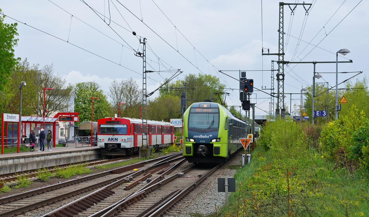 ET 5.07 der Nordbahn fährt am 16.04.2024 mit einer RB in Richtung Itzehoe aus Elmshorn aus, rechts wartet der AKN-VTA 66 auf Fahrgäste nach Ulzburg Süd. In Elmshorn zweigt die Marschbahn nach Westerland von der Strecke nach Flensburg/Kiel ab. Mit nur drei Bahnsteiggleisen (und dem Kopfgleis der AKN) geht es hier ziemlich beengt zu, daher ist ein Neubau der Bahnstation mit zwei Mittelbahnsteigen etwa 200 m südlich des heutigen Bahnhofs ab Ende 2031 geplant. Zu den VTA der AKN sei ergänzend angemerkt, dass diese nur noch auf der Linie zwischen Elmshorn und Ulzburg Süd verkehren - und dies wahrscheinlich nicht mehr allzu lange, denn durch die Umstellung auf Akkutriebwagen im Nordnetz werden LINT frei, die die VTA ersetzen können.