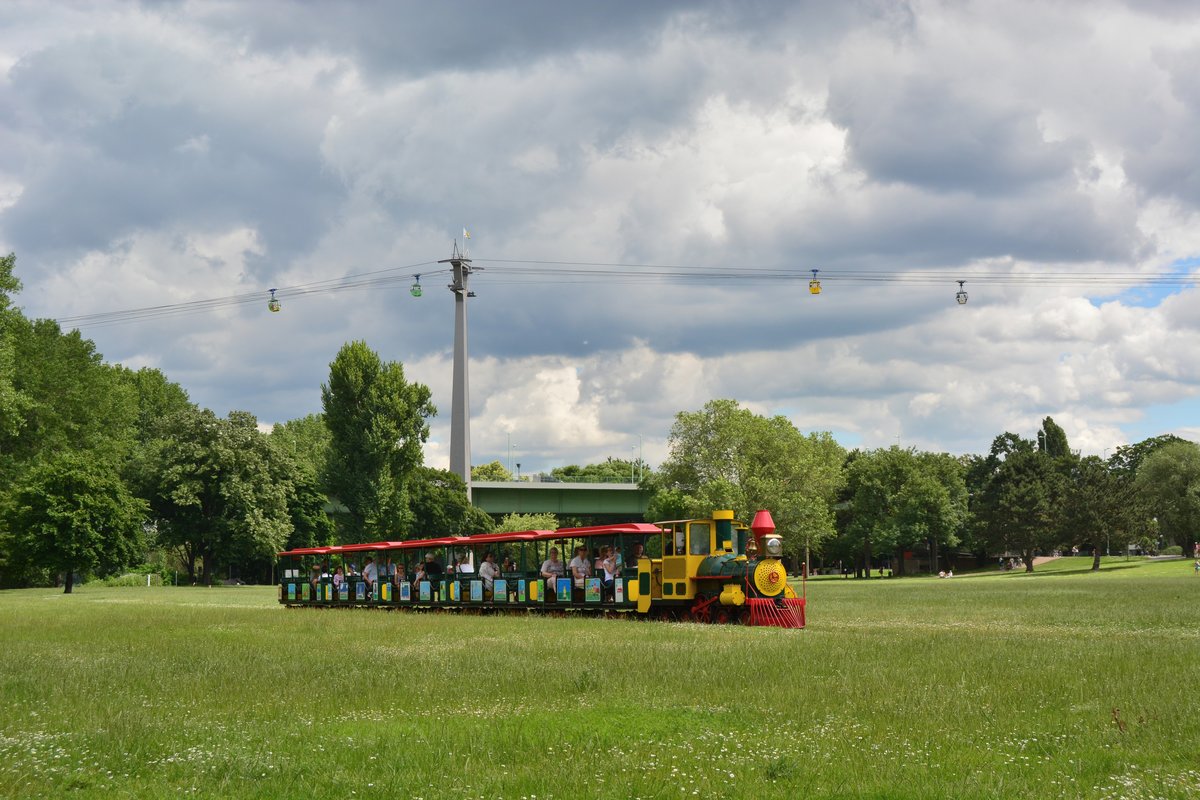 Etwas abseits des Trubels fährt die Parkeisenbahn im Rheinpark. Zur Bundesgartenschau 1971 erbaut fährt sie bis heute durch den Rheinpark und erfreut große und kleine Besucher. Im Hintergrund ist die Kölner Seilbahn zu sehen. 

Köln 16.06.2019