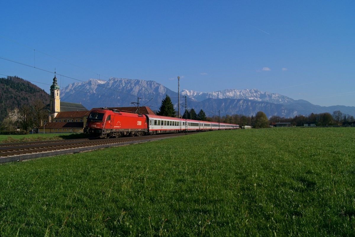 Eurocity 84 mit 1216 008 an der Spitze war am 08.04.2017 auf dem Weg von Rimini nach München und hat gerade den Bahnhof Kufstein verlassen, als er das Kloster Reisach passiert. Im Hintergrund ist das Kaisergebirge zu sehen. 