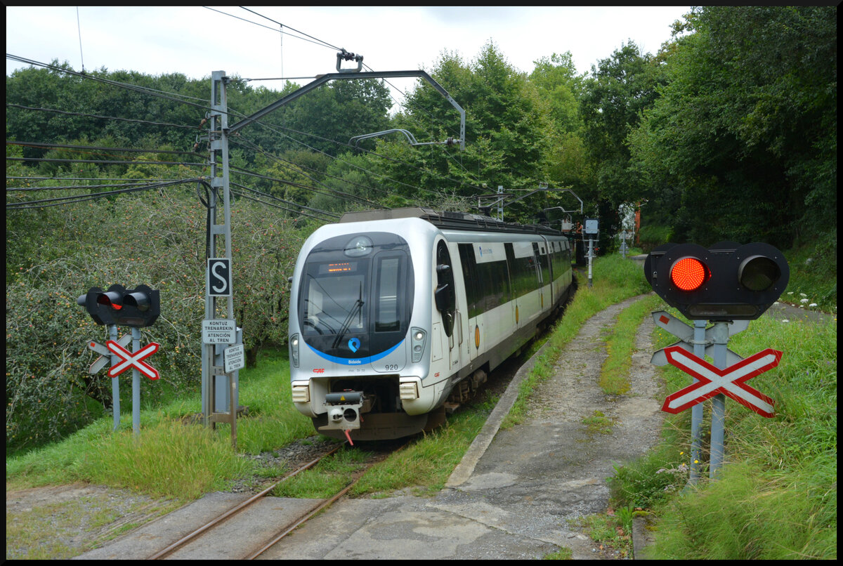 Euskotren Trena: Nahe des ehem. Bf. Txokoalde passiert ein CAF-Triebzug der BR 900 pünktlich einen Feldweg-BÜ in Richtung Bilbao Matiko. 16.08.2023