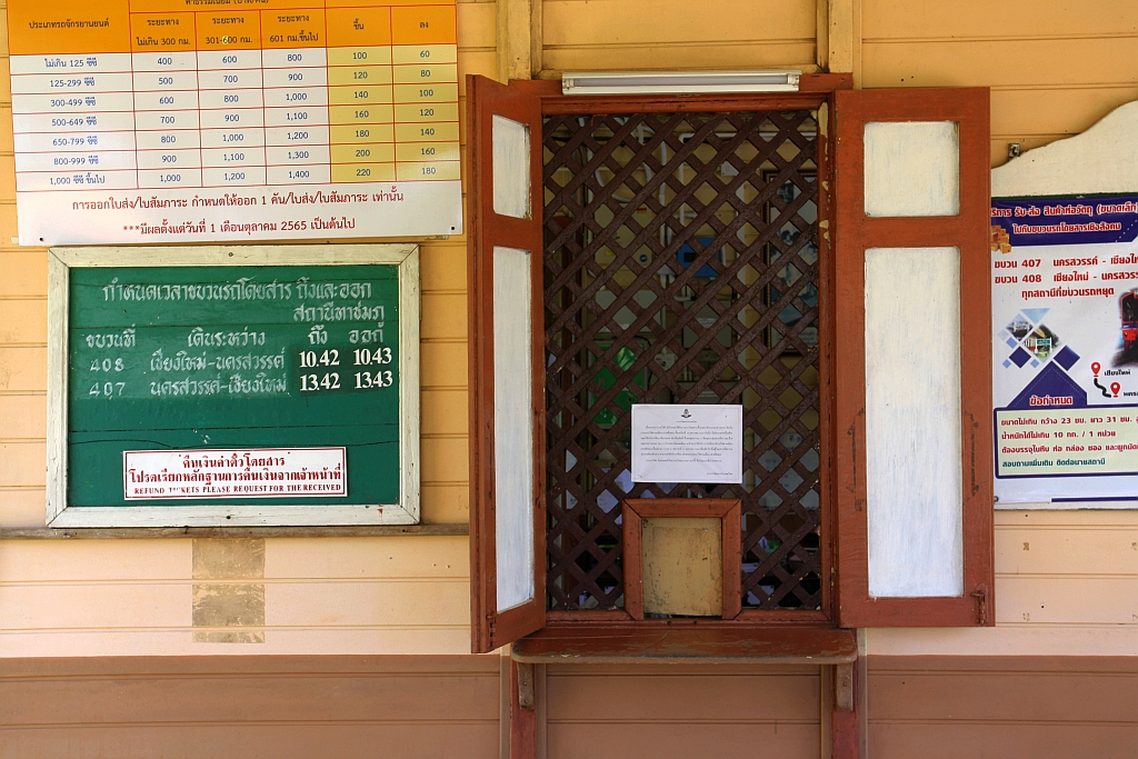 Fahrkartenschalter und eine recht überschaubare Abfahrtstafel der Tha Chomphu Station am 22.März 2023. - Über der Abfahrtstafel sieht man die Preisliste für Motorräder, gestaffelt nach Hubraum und Entfernung, sowie in den beiden letzten Spalten die Kosten für's Ein- und Ausladen.