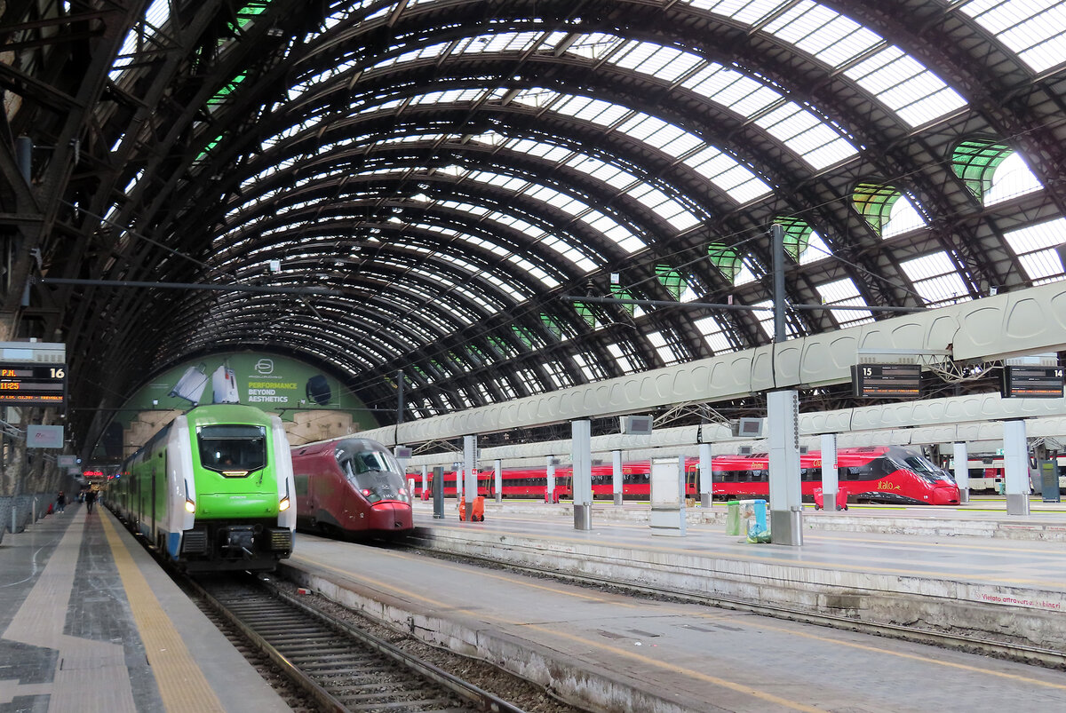 Farbige Züge im Bahnhof Milano Centrale: ein grün-weisser Regionalzug und zwei Hochgeschwindigkeitszüge warten auf die Abfahrt. Milano, 25.4.2023