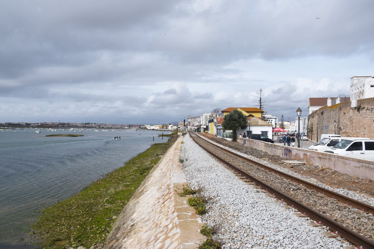 FARO (Distrikt Faro), 12.03.2022, Linha do Algarve kurz vor dem Bahnhof Faro; rechts ist die Mauer um die Altstadt zu sehen; Aufnahme von einem Bootsanleger, der über das Gleis führt