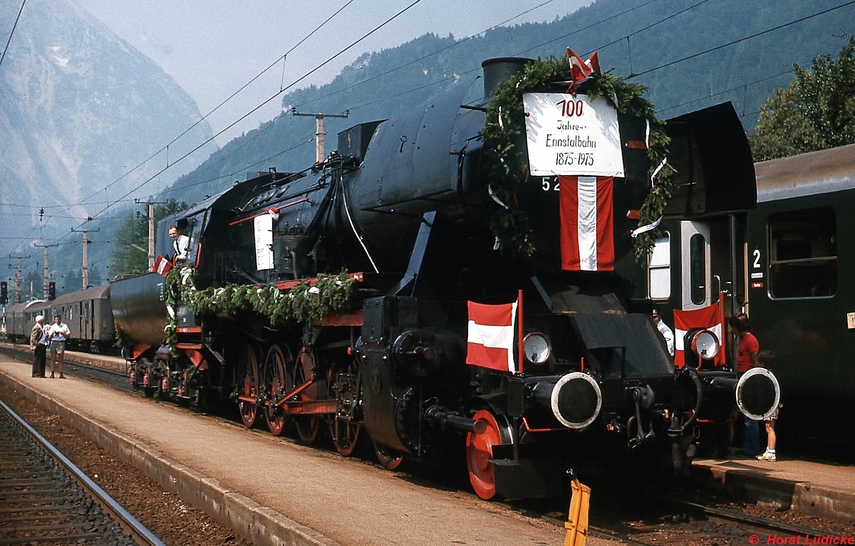 Festlich geschmückt präsentiert sich die 52.7593 anlässlich des 100-jährigen Jubiläums der Ennstalbahn am 15.08.1975 in Stainach-Irdning. Gerade hat sie den Sonderzug aus Schladming gebracht und setzt jetzt für die Rückfahrt um.