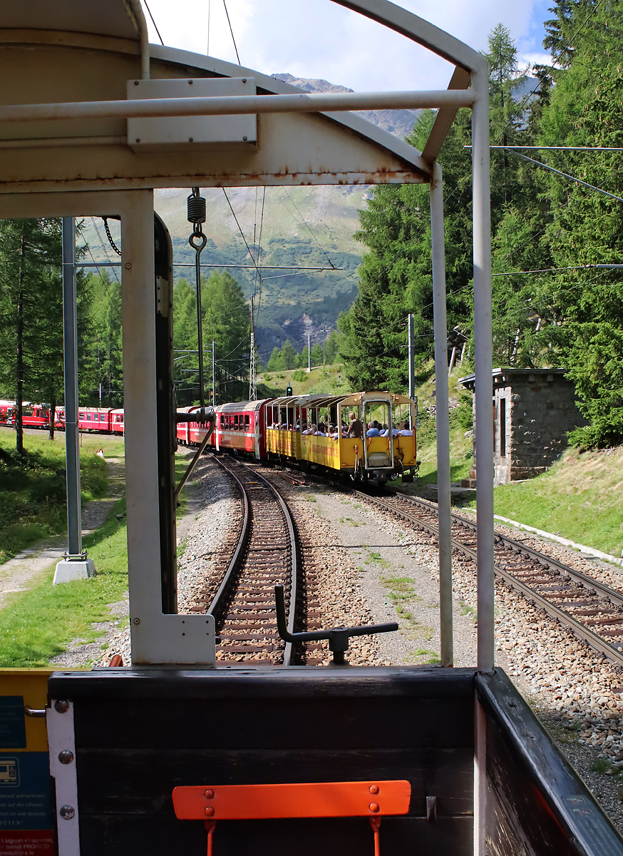 Foto aus dem offenen Panoramawagen am Zugschluss: Regionalzug von St. Moritz nach Tirano kreuzt den Regionalzug der Gegenrichtung in einer Dienststation zwischen Alp Grüm und Cavaglia. Cavaglia, 21.8.2023
