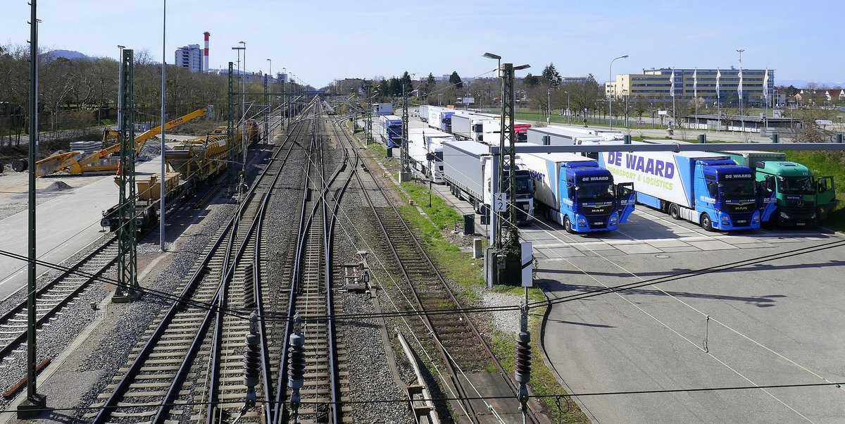 Freiburg, Blick von der Brücke über die Gleise des ehemaligen Güterbahnhofes, links ein Bauzug, rechts warten die LKW auf die Bahnverladung, März 2021