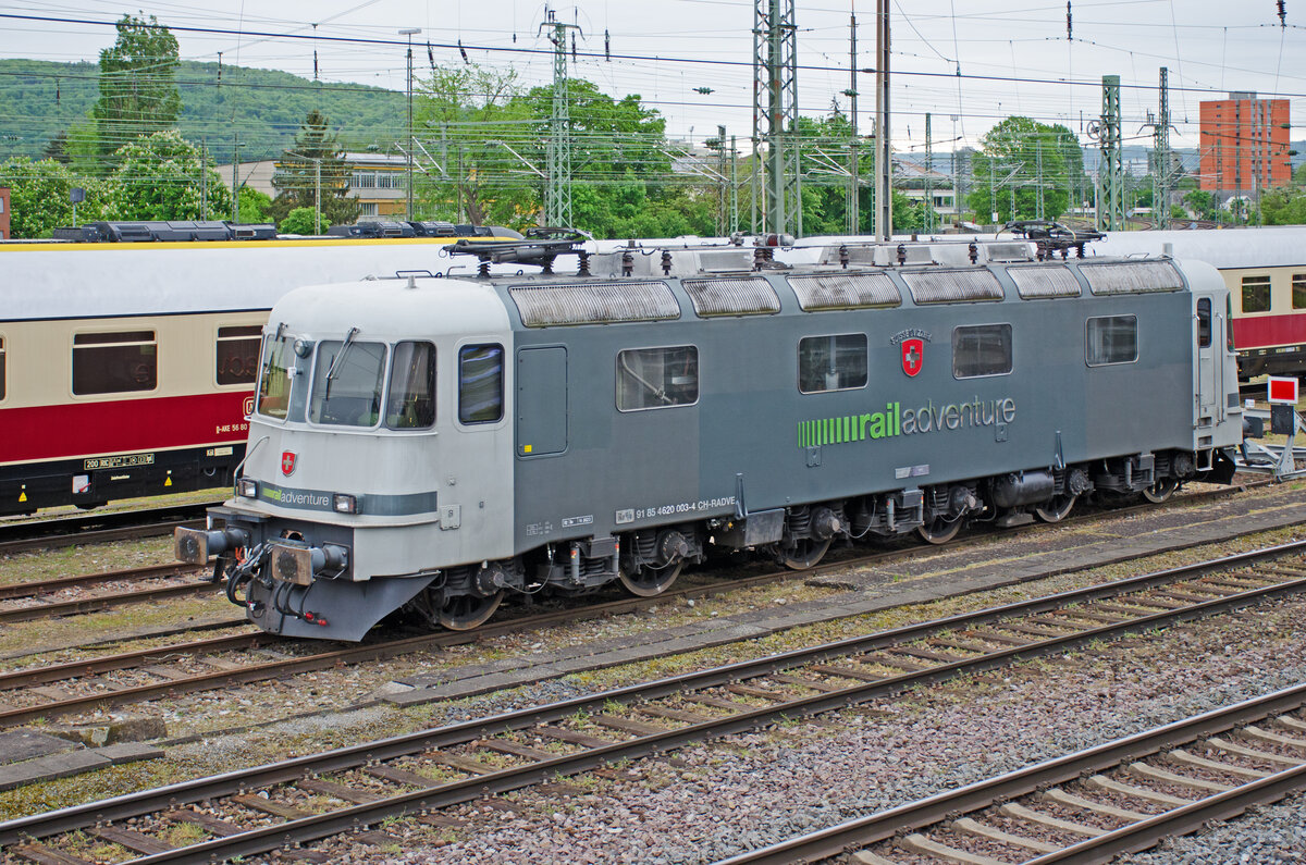 Freitag den 03.05.2024 um 08:23 Uhr in Basel. Im Bahnhof  Basel Bad Bf“ (DB Bahnhof auf Schweizer Gebiet) steht auf der Südseite des Personenbahnhofs in einem der Stumpengleise / Stumpfgleise eine abgestellte SBB Re 6/6. Ursprungsnummer: 11603, Ursprungswappen: Wädenswil. Heutige Bezeichnung: Re 620, 91 85 4620 003-4 CH-RADVE, Erbauer: SLM und BBC, Inbetriebsetzung: 1972, Stundenleistung Total: 10'600 PS, Achsfolge: Bo’Bo’Bo’. Ursprünglich besass diese Maschine beim mittleren Drehgestell als Sekundärfedern Luftfedern. Bei der endgültigen Abgabe an die SBB erhielten sie wieder Schraubenfedern weil die Luftfedern keine bedeutenden Vorteile zeigten. RADVE bedeutet railadventure. Die RailAdventure GmbH, Fahrzeughalterkennzeichnung RADVE, ist ein deutsches Eisenbahnverkehrsunternehmen mit Sitz im Münchner Stadtteil Neuhausen-Nymphenburg. RailAdventure ist ein neutraler Dienstleister für die Bahnindustrie. Als Wappen trägt die Re 620 heute das Schweizerwappen. Auf der hier abgebildeten Seite steht über dem Wappen  Suisse / Svizzera“ während auf der anderen Seite über dem Wappen  Schweiz / Svizra“ geschrieben steht.  Statt die Lokomotive wie üblich vor der NVR Nummer mit  Re 620“ zu bezeichnen wurde ein  altes“ Bezeichnungsschild von früher vor die NVR Nummer geschraubt. Irgendwie haben die  Neugestalter“ Humor und Fantasie bewiesen. Koordinaten GMS (Grad, Minuten, Sekunden): N 47° 33’ 50.7’’ O 7° 36’ 35.3’’