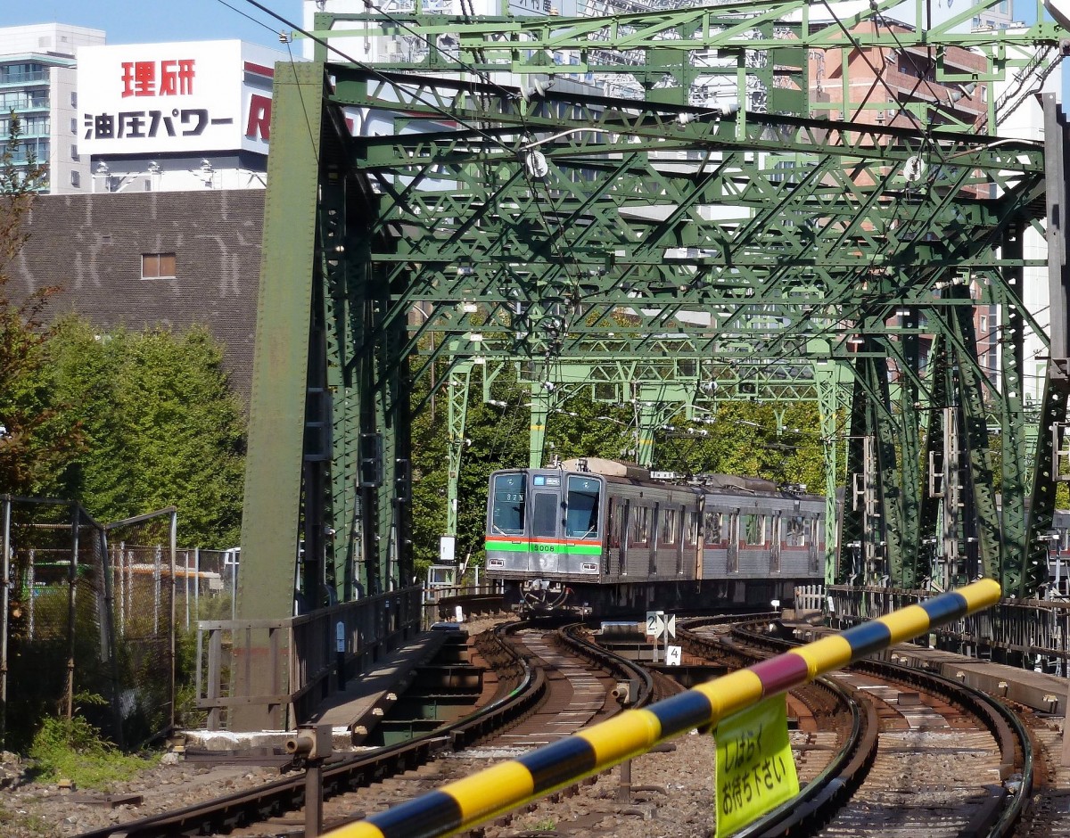 Fremde Züge auf der Keikyû-Linie: Die Chiba New Town –Bahn. Zug 9011 auf der Brücke über die JR-Geleise in Tokyo-Shinagawa. 28.Oktober 2011. Der Text am Schild an der Schranke übersetzt sich sinngemäss als  Bitte haben Sie etwas Geduld . 