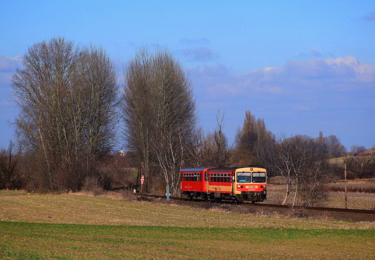 Früh-Frühling-Idyll auf der Bakonybahn: die 117 296 (Bzmot 296) als Zug 39514 von Győr nach Veszprém bei Écs.
Écs, 26.02.2022.