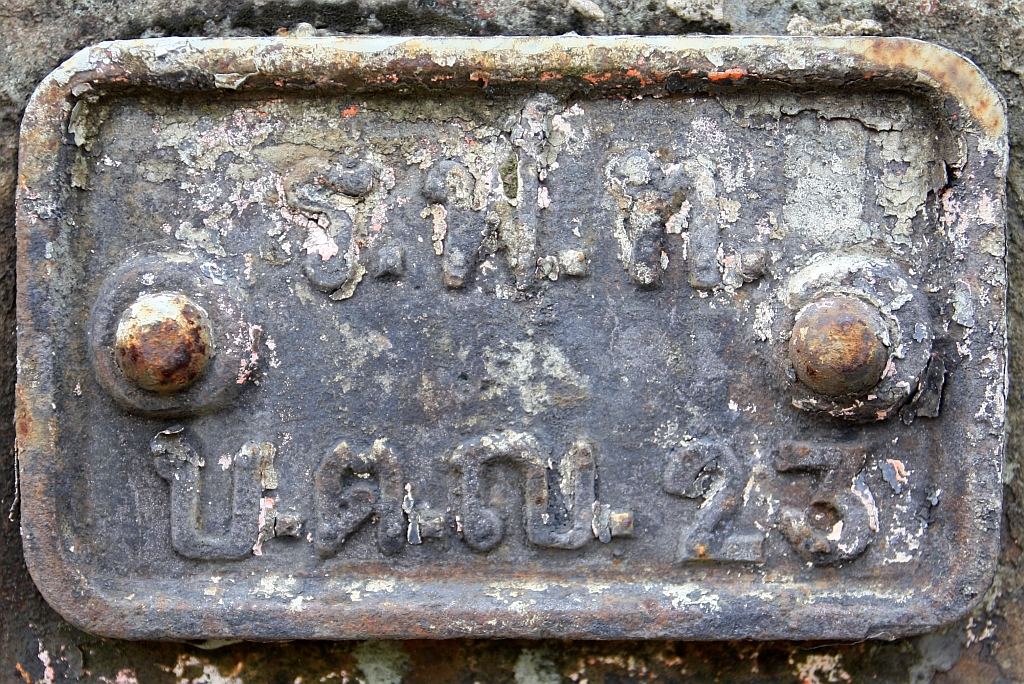 Früher erhielten die Güterwagen der SRT beidseitig angenietete Gussschilder auf denen das Eigentümerkürzel, das Gattungskürzel und die Fahrzeugnummer erkennbar sind. - Fahrzeugnummernschild des 
บ.ต.ญ.23 (บ.ต.ญ.=B.C.G./Bogie Covered Goods Wagon, Baujahr 1943) am 22.März 2025 in der Den Chai Station.