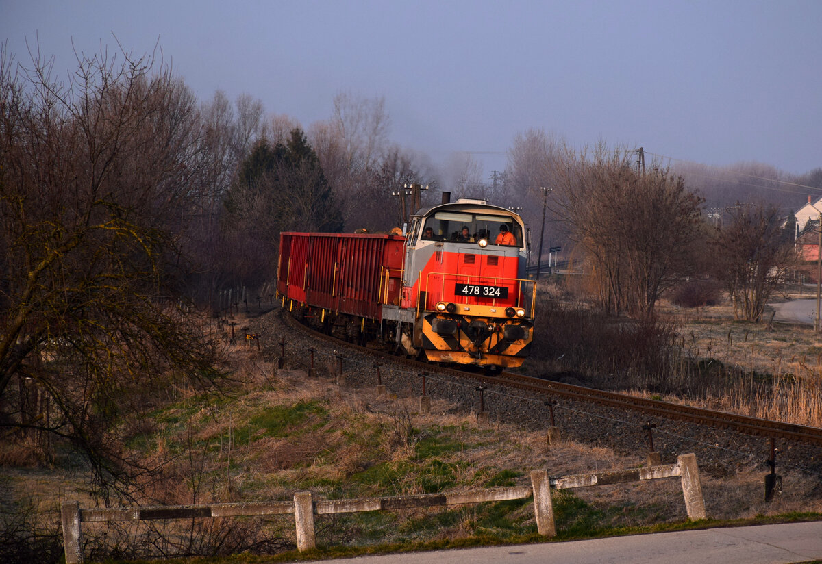 Frühmorgen, -8 Grad im März. Die 478 324 (M47 1324) mit dem Verschubgüterzug von Celldömölk nach Holzwerk Franciavágás kurz vor der Ankunft in Bf. Pápa. 
Pápa, 04.03.2022.