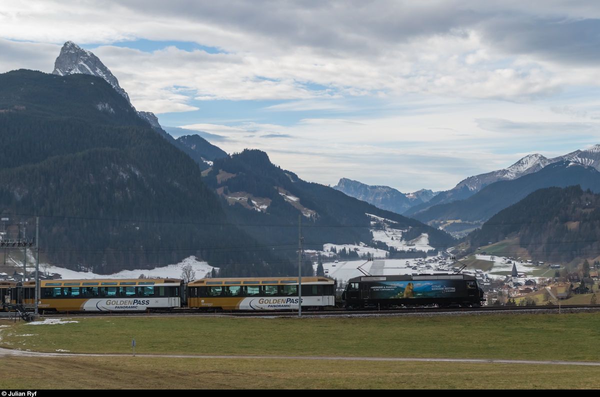 Für einmal ein Vorteil der Fotowolke: Die Stelle bei Gruben wäre um diese Tageszeit voll im Gegenlicht.
Die  Murmeli-Lok  Ge 4/4 8003 zieht am 24. Dezember 2015 einen GoldenPass Panoramic in Richtung Zweisimmen. Im Talboden ist der Flugplatz und das Dorf Saanen zu sehen.