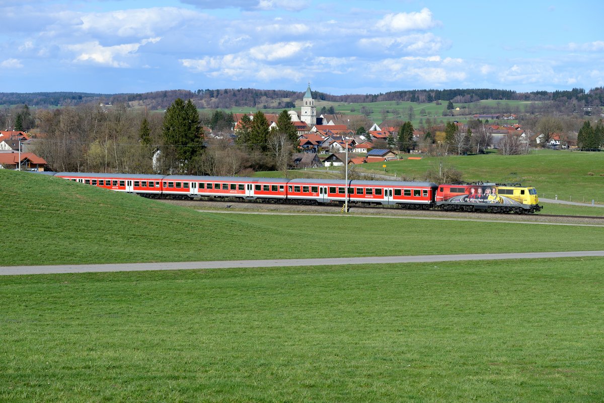  Für Menschen unterwegs  ist die ADAC Werbelok 111 024 und schiebt hier gerade die RB 59546 nach München an der Ortschaft Polling vorbei. Die spätgotische Klosterkirche dominiert das Ortsbild (13. April 2013).