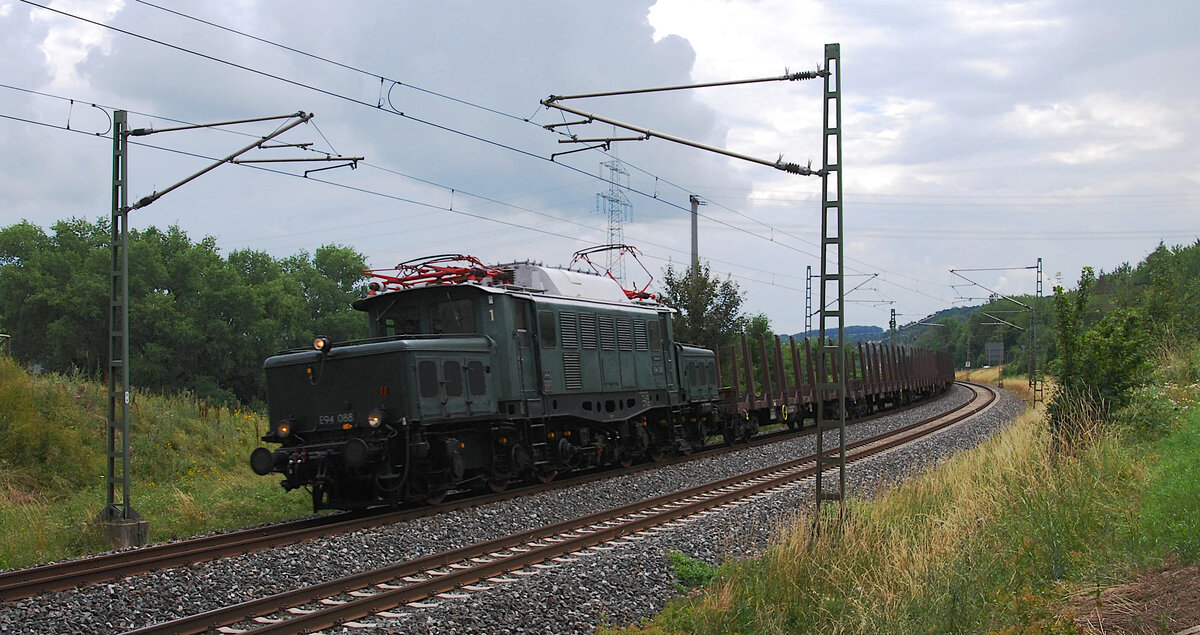 Für Sonntag, 04.07.2021, hatte die Elektrische Zugförderung Württemberg (EZW) über Facebook einen  Fotogüterzug  angekündigt. Die Fahrtroute ging von Regensburg über Nürnberg, Ansbach, Würzburg, Aschaffenburg, Gießen nach Marburg/Lahn. Gegen Mittag konnte das mit etwas mehr als einer Stunde verspätet dahin schleichende Krokodil E94 088 mit seinem Ganzzug leerer Rungenwagen bei Goßmanndorf nahe Ochsenfurt am Main eingefangen werden.

