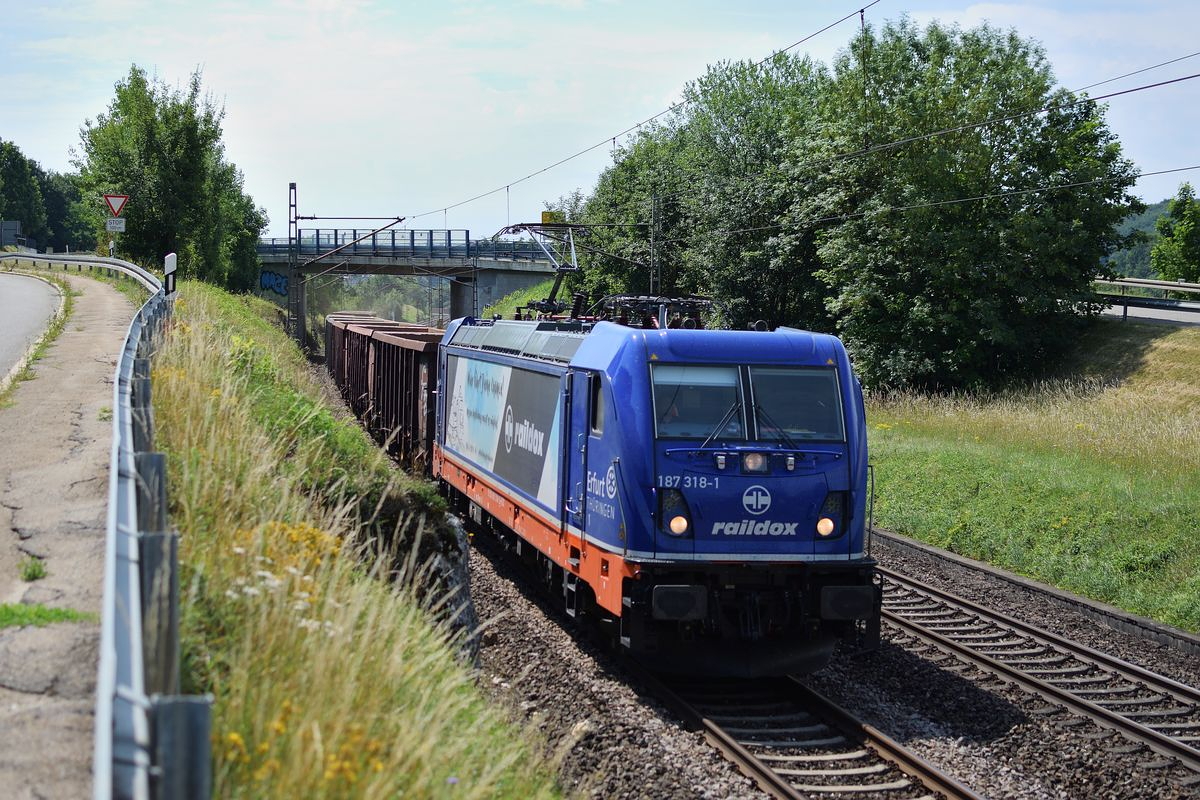 Gegen Mittag des 4. Juli 2018 bringt 187 318 einen weiteren Zug aus leeren Hochbordwagen nach Amstetten. Hier fährt sie durch in Lonsee.