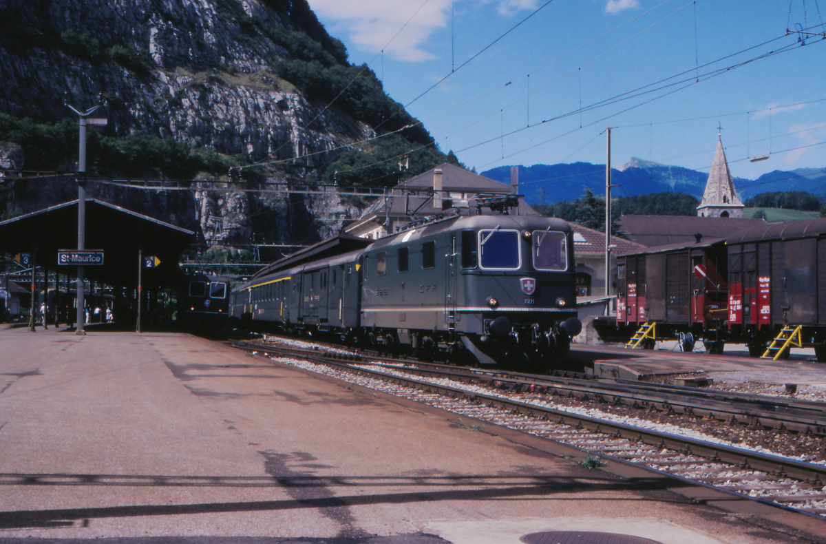 Gerade ist die Re4/4 II 11271 der SBB mit einem Schnellzug Romanshorn - Zürich - Biel - Lausanne - Brig in Saint Maurice an der Rhone angekommen. Die Lokomotive ist klassisch grün, der Schnellzug besteht aus Einheitswagen II. Die Lok hat in Zürich übernommen und macht mit dem Zug eine Rundfahrt durch die Schweiz - ob wohl jemals ein Fahrgast den ganzen Laufweg mitgefahren ist?
Saint Maurice, 1. Juli 1988; Canon AE-1, Canoscan, Gimp