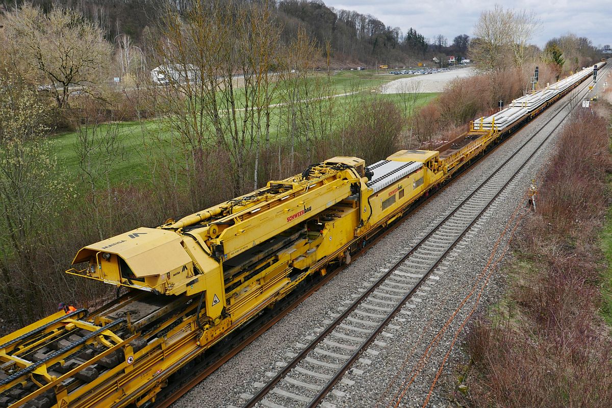 Gleisumbauzug MATISA P 95 (99 80 9211 007-6 D-SBAU) zwischen Biberach (Riß) und Warthausen - Der Portalkran des SCHWEERBAU-Umbauzuges befördert neue Schwellen von einem Flachwagen am Anfang des Zuges zum Maschinenteil, das die alten gegen die neuen Schwellen austauscht (26.03.2019).
