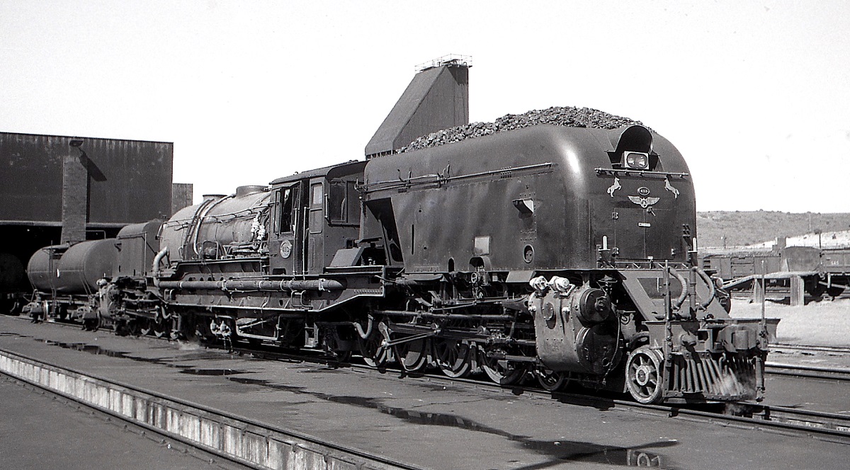 GMAM 4113 der SAR im November 1976 im Depot Mosselbaai. Bei diesen Lokomotiven der Bauart Garratt werden zwei Triebwerkseinheiten durch einen Brückenrahmen, auf dem Kessel und Führerhaus untergebracht sind, verbunden. Zwischen 1952 und 1958 bauten Henschel, Beyer-Peacock und North British insgesamt 120 GMA (mit geringeren Vorratsbehältern) und GMAM mit der Achsfolge (2D1')(1D2') h4 für die SAR. Zum Zeitpunkt der Aufnahme war die Strecke Mosselbaai - George - Oudshoorn noch fest in der Hand dieser imposanten Lokomotiven. Die letzten schieden 1984 bei der SAR aus, einige wurden noch an Kohleminen und nach Simbabwe verkauft.